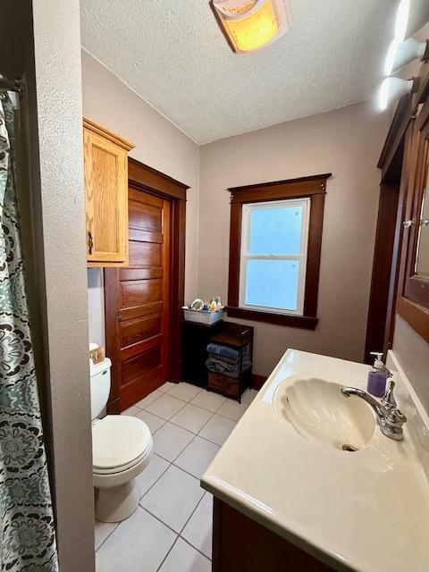 bathroom with tile patterned flooring, vanity, toilet, and a textured ceiling