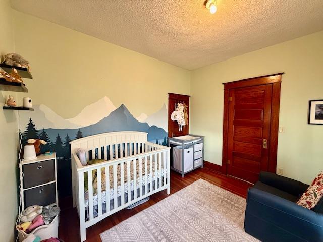 bedroom featuring wood finished floors, a crib, and a textured ceiling