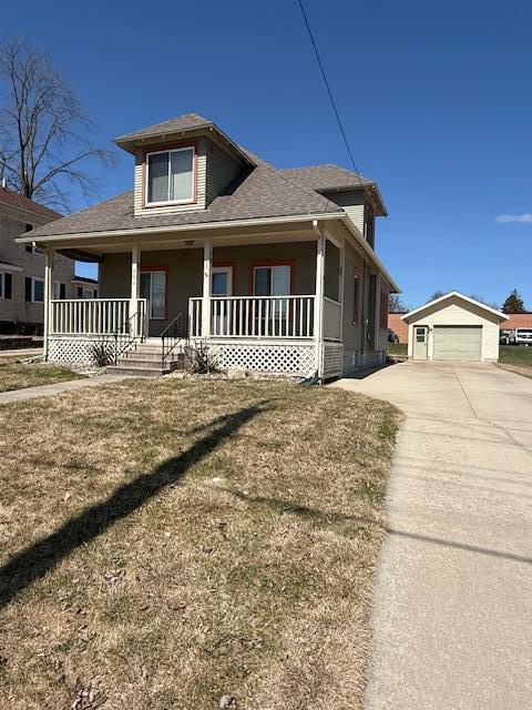 view of front of property with a garage, a front yard, roof with shingles, an outbuilding, and a porch