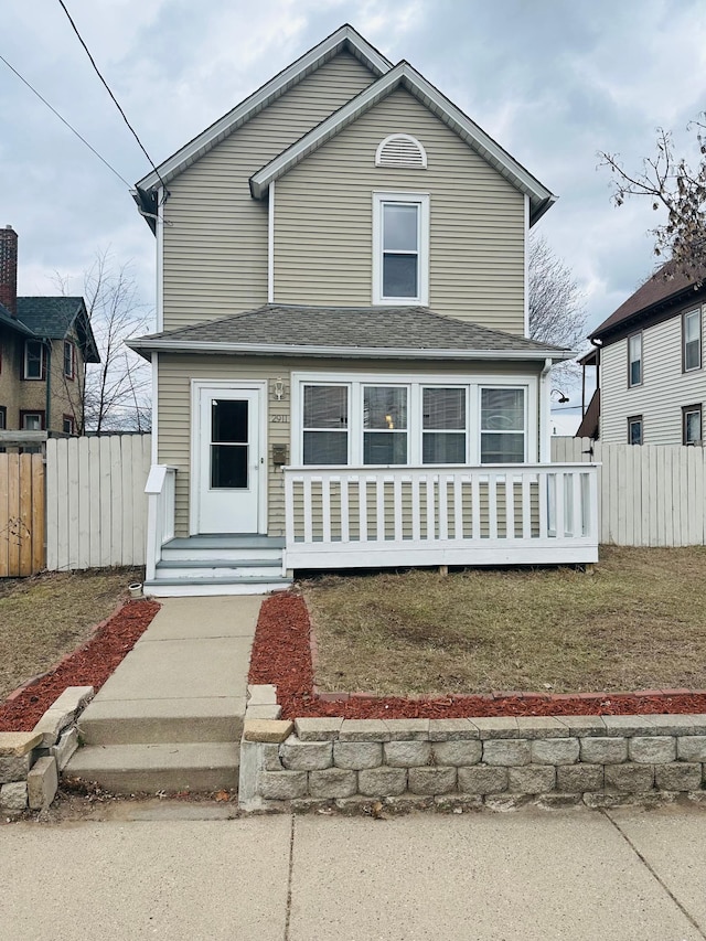 view of front facade featuring roof with shingles and fence