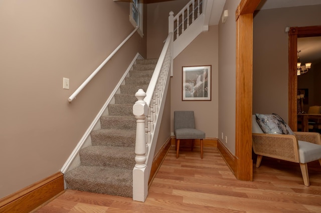 stairs with wood finished floors, a notable chandelier, and baseboards