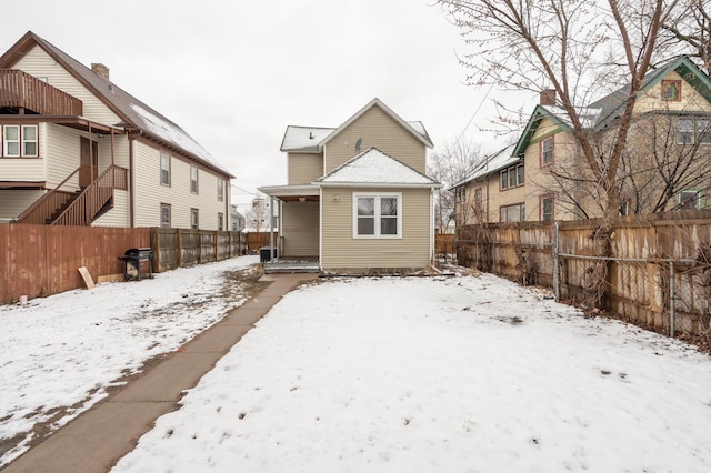 snow covered back of property featuring central air condition unit and fence private yard