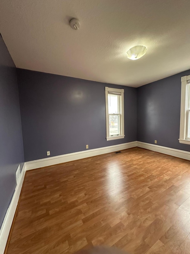 unfurnished room featuring visible vents, baseboards, wood finished floors, and a textured ceiling