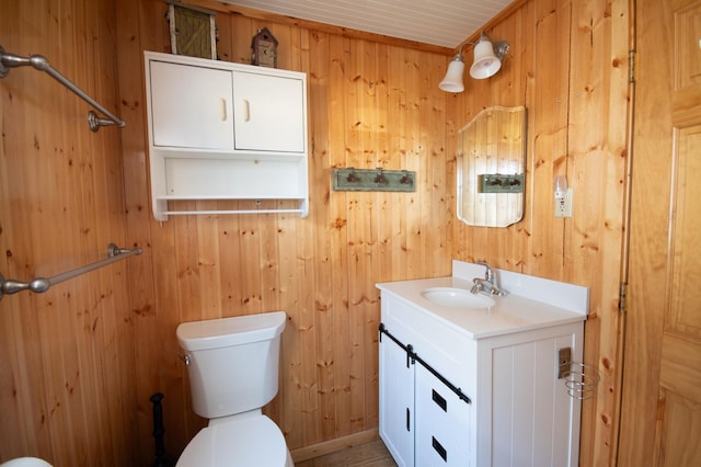 bathroom with toilet, wood walls, and vanity