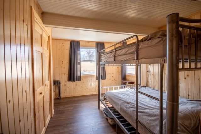 bedroom with dark wood finished floors, wood walls, and baseboards