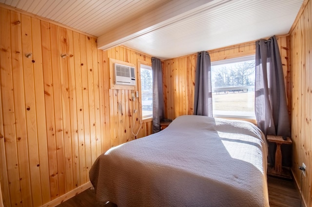 bedroom with dark wood finished floors, wood walls, and multiple windows