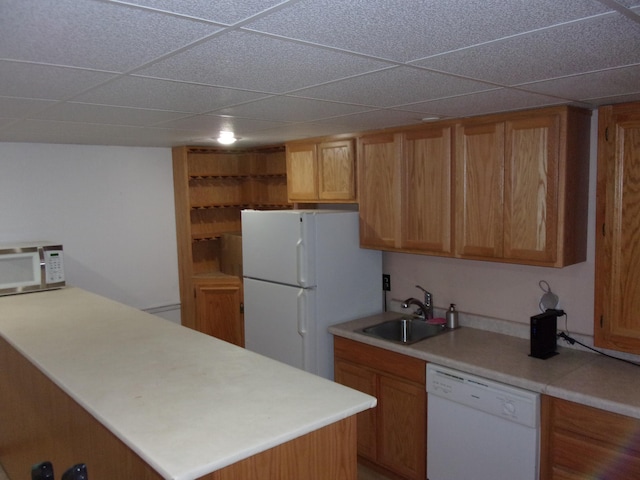 kitchen with white appliances, a sink, a peninsula, light countertops, and a drop ceiling