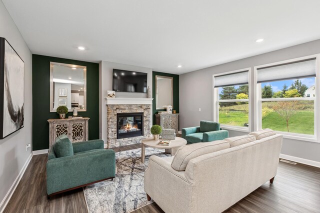 living area featuring baseboards, dark wood-style flooring, a stone fireplace, and recessed lighting