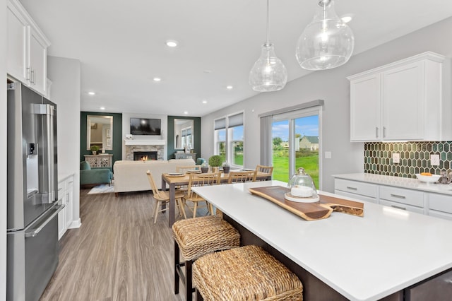 kitchen featuring white cabinets, stainless steel fridge with ice dispenser, light countertops, a stone fireplace, and decorative backsplash