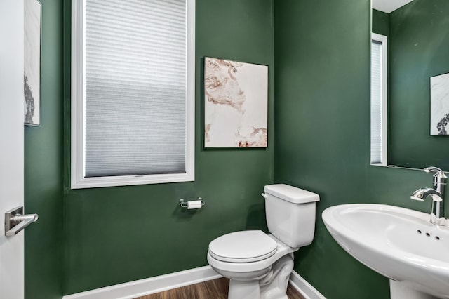 half bath with toilet, wood finished floors, a sink, and baseboards