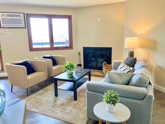 living room with a glass covered fireplace, baseboards, an AC wall unit, and wood finished floors