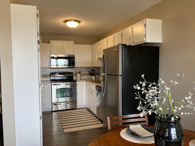 kitchen with decorative backsplash, light countertops, white cabinets, dark wood finished floors, and stainless steel appliances