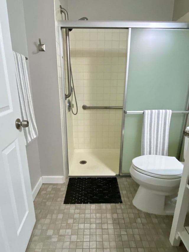 bathroom with toilet, tile patterned floors, baseboards, and a stall shower