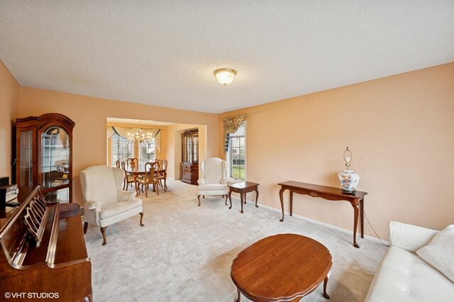 living area featuring an inviting chandelier, carpet floors, baseboards, and a textured ceiling