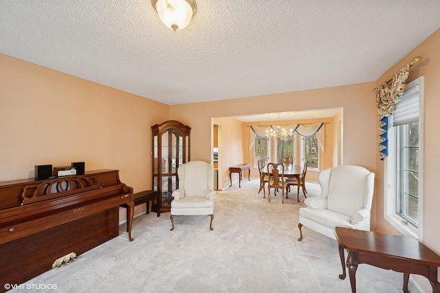 sitting room with plenty of natural light, light colored carpet, a textured ceiling, and a notable chandelier