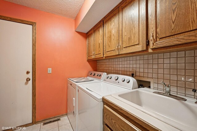 clothes washing area with washing machine and dryer, a textured ceiling, a sink, cabinet space, and light tile patterned floors