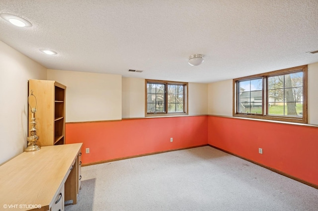 unfurnished office featuring carpet floors, a textured ceiling, visible vents, and a healthy amount of sunlight