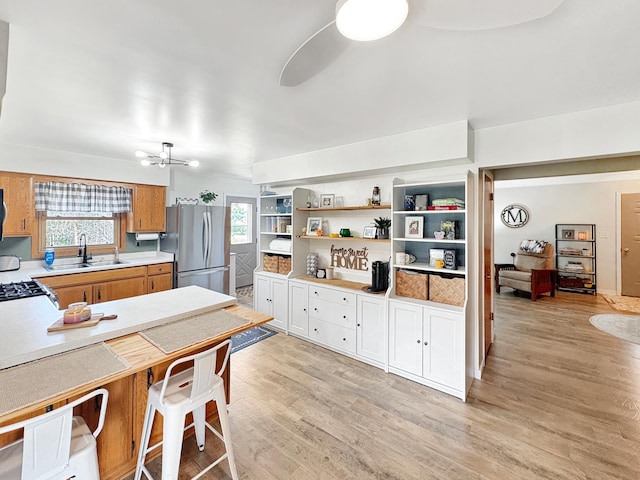 kitchen with open shelves, light wood-type flooring, a sink, light countertops, and freestanding refrigerator