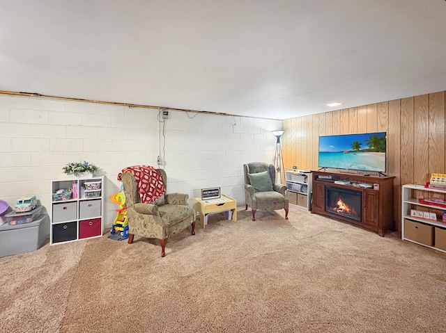 living room featuring carpet floors, concrete block wall, a glass covered fireplace, and wooden walls