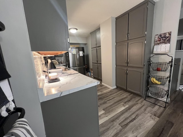 kitchen featuring light countertops, gray cabinets, baseboards, freestanding refrigerator, and wood finished floors