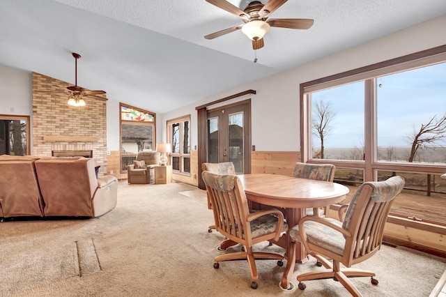 carpeted dining room featuring wainscoting, a ceiling fan, a brick fireplace, and vaulted ceiling