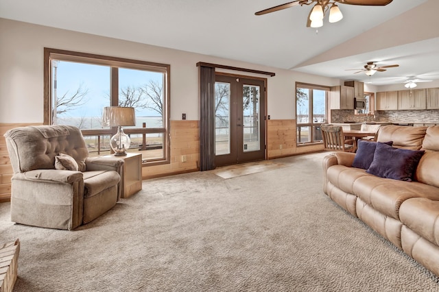 living room with a wainscoted wall, light colored carpet, vaulted ceiling, and ceiling fan