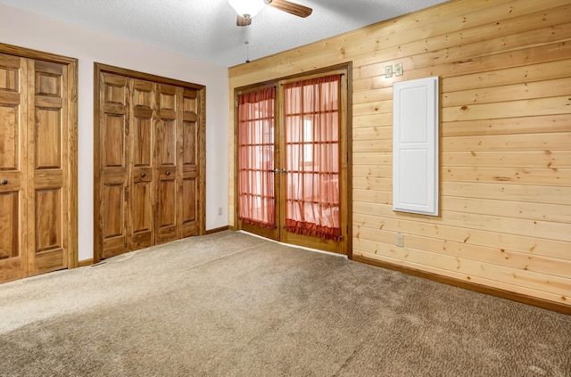 unfurnished bedroom with wooden walls, carpet floors, a textured ceiling, and baseboards