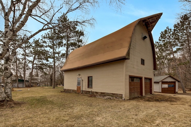view of home's exterior featuring an attached garage, a gambrel roof, a lawn, and an outdoor structure