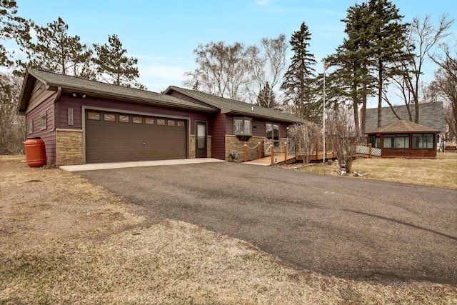 view of front facade with an attached garage, driveway, stone siding, and a wooden deck