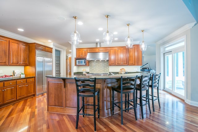 13980 Emerald Rdg, Minnetonka, MN 55305 - kitchen featuring built in appliances, under cabinet range hood, crown molding, brown cabinetry, and recessed lighting