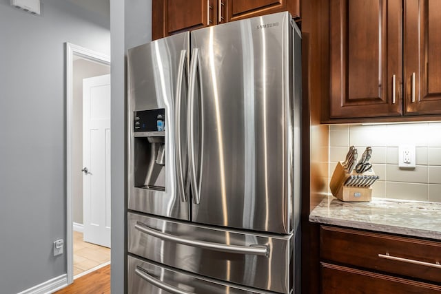 kitchen featuring backsplash, baseboards, light stone counters, and stainless steel fridge with ice dispenser