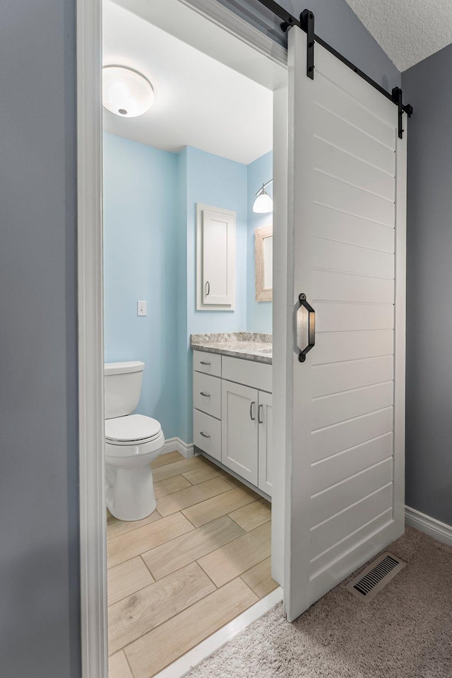 bathroom with vanity, toilet, baseboards, wood tiled floor, and visible vents