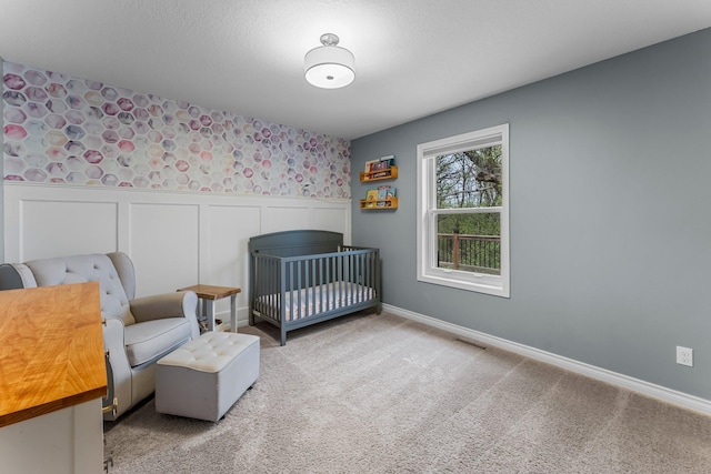 carpeted bedroom featuring visible vents, wainscoting, baseboards, wallpapered walls, and a nursery area