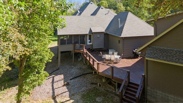 rear view of property featuring a wooden deck, a sunroom, and a shingled roof