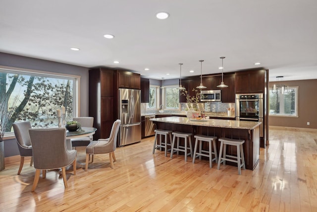 kitchen with light wood finished floors, a center island, appliances with stainless steel finishes, and decorative backsplash