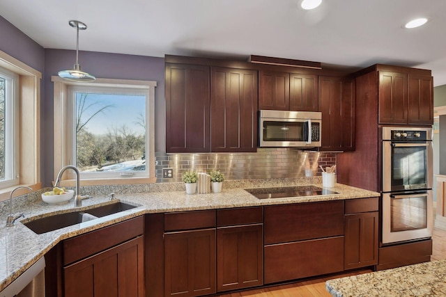 kitchen with light stone countertops, appliances with stainless steel finishes, a sink, hanging light fixtures, and decorative backsplash