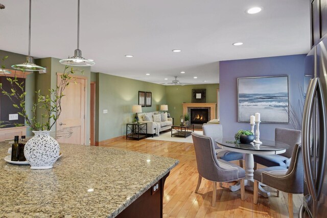 kitchen with a lit fireplace, freestanding refrigerator, a ceiling fan, light stone countertops, and light wood finished floors
