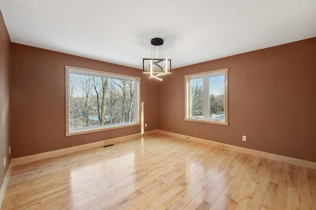 unfurnished dining area with a wealth of natural light, light wood-style floors, visible vents, and an inviting chandelier