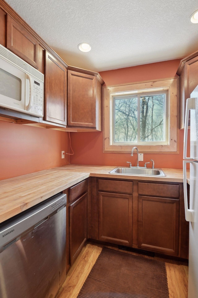 kitchen featuring white appliances, light wood-style floors, a textured ceiling, and a sink