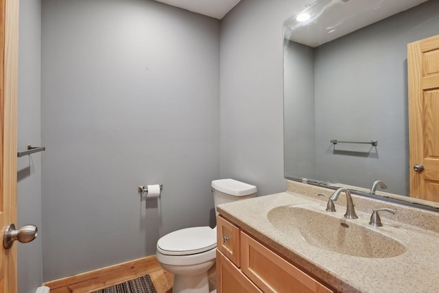 half bathroom featuring toilet, vanity, and wood finished floors
