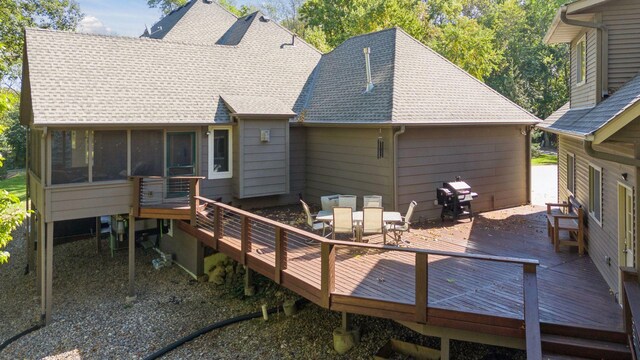 back of house with a wooden deck, a sunroom, outdoor dining area, and roof with shingles