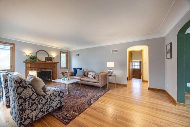living room featuring light wood finished floors, a brick fireplace, baseboards, visible vents, and arched walkways