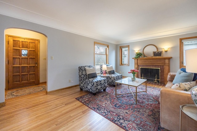 living room featuring crown molding, wood finished floors, a brick fireplace, baseboards, and arched walkways
