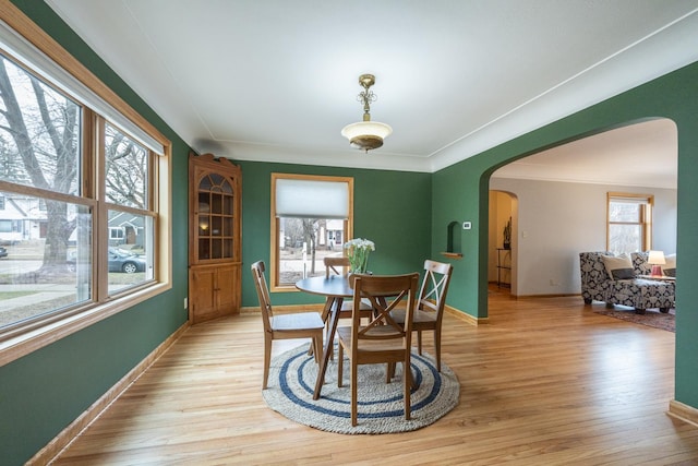 dining area with light wood-style flooring, arched walkways, crown molding, and baseboards