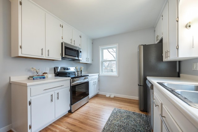 kitchen featuring white cabinetry, light countertops, light wood-type flooring, baseboards, and appliances with stainless steel finishes
