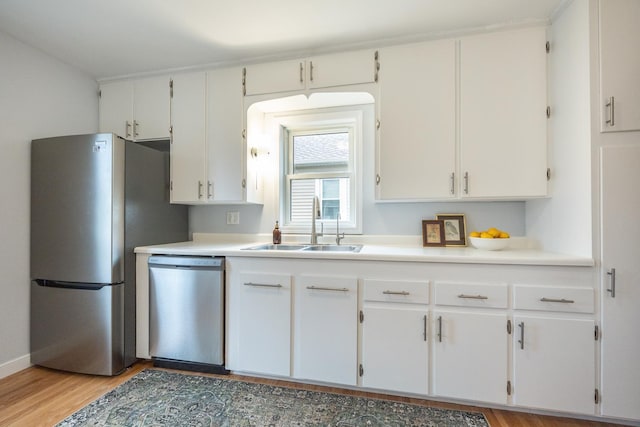 kitchen featuring white cabinetry, a sink, stainless steel appliances, and light wood-style floors