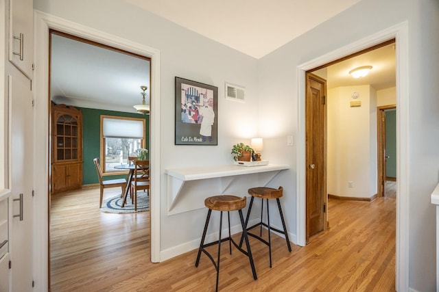 kitchen featuring baseboards, a breakfast bar area, visible vents, and light wood-style flooring