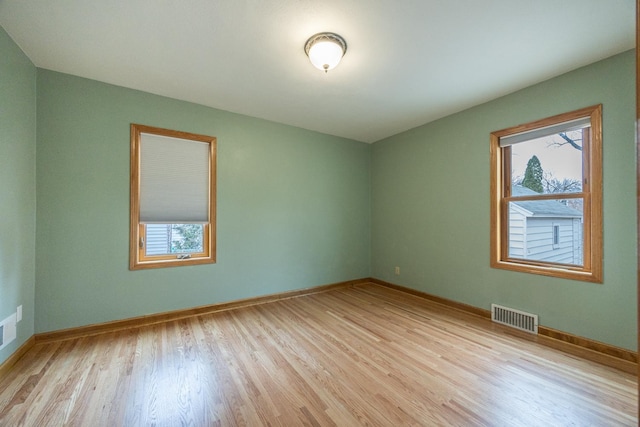 unfurnished room featuring light wood finished floors, baseboards, visible vents, and a healthy amount of sunlight