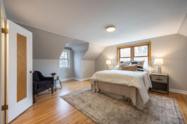 bedroom with light wood finished floors, baseboards, and lofted ceiling