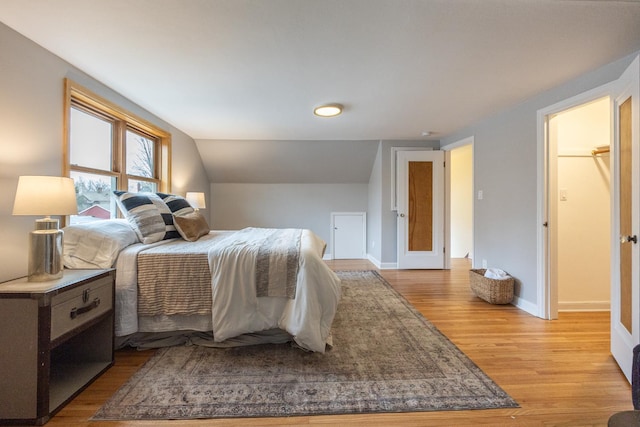 bedroom with baseboards, light wood-type flooring, and vaulted ceiling